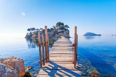 a wooden walkway leading to an island in the middle of the ocean with blue water