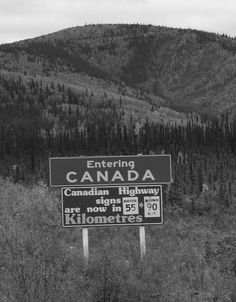 a black and white photo of a road sign in front of a mountain with trees