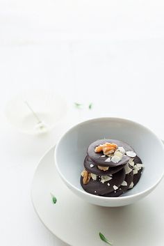 a white bowl filled with chocolate covered cookies on top of a white plate next to flowers