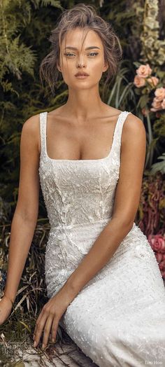 a woman in a white dress sitting on the ground next to some plants and flowers