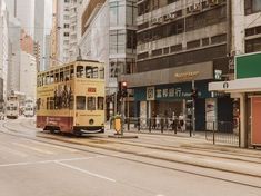 a yellow double decker bus driving down a street next to tall buildings and people walking on the sidewalk