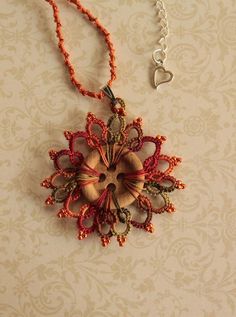 an orange and red beaded necklace hanging from a chain on a beige wallpapered surface