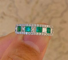 an emerald and diamond ring on someone's finger