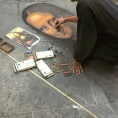 a man sitting on the ground next to a drawing of a man's face