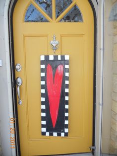 a yellow door with a red heart painted on the front and side panels, next to a black and white checkered door frame