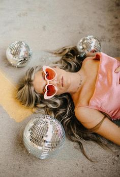 a woman laying on the ground next to two disco balls with her eyes closed,