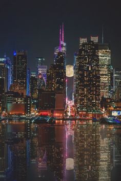 the city skyline is lit up at night and reflecting in the water with bright lights