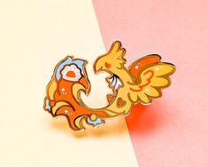 an orange and blue bird brooch sitting on top of a pink and white background