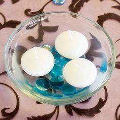 three white candles are in a glass bowl