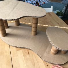 a table made out of cardboard sitting on top of a wooden floor next to a person's hand