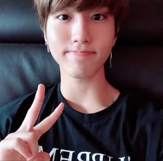 a young man sitting in a chair making the peace sign with his hand while wearing a black shirt