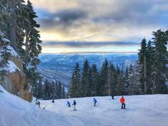 several people skiing down a snow covered slope with mountains in the background and clouds in the sky