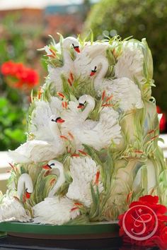 there is a cake decorated with swans and flowers on top of a table in front of some potted plants