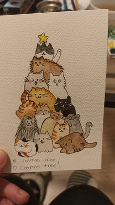 a person holding up a card with many cats on it in front of a christmas tree