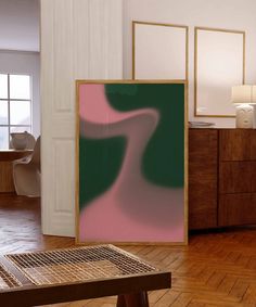 an abstract painting is on display in a room with wooden floors and white walls, next to a coffee table