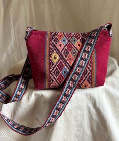 Handwoven Small Handbag of Red/Multicolor Stripes with woven details in stripes  of Wool and Alpaca, handwoven strap and zipper closure.  Black cotton lining with Zipper opening at top  Height 5.5" and 8" across at the top Gusset Bottom at the bottom of the handbag is 6"x2.25" 7.5" Zipper at the top  Adjustable Shoulder Strap are 1.15" across and 47" total length.  This handbag can be worn as a crossbody handbag as well. 90% wool and 10% alpaca, all natural vegetable dyed.  Produced one at a time by women and men located in Chahuaytire and  Chincero, north of Cusco, Peru. Hangtag indicates the person who made this handbag, Agueda Huayllani Holgado.  The weaver has gathered the wool, spun and dyed the yarn, and then woven the textile for the handbag. For more info about the cooperative in P Traditional Red Woven Shoulder Bag, Red Woven Festival Bag, Handwoven Red Shoulder Bag For Travel, Red Handwoven Shoulder Bag For Travel, Red Handwoven Shoulder Bag For Everyday Use, Red Handwoven Shoulder Bag, Festival Red Woven Bag, Artisan Red Rectangular Shoulder Bag, Artisan Red Woven Shoulder Bag