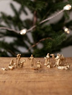 gold figurines sitting on top of a wooden table next to a christmas tree