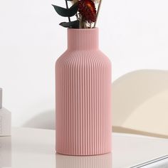 a pink vase sitting on top of a white table next to a bottle with flowers in it