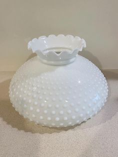 a white glass vase sitting on top of a table next to a wall and floor