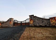 a stone gate with christmas decorations on it and a driveway leading up to the entrance