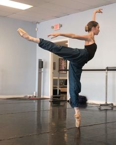 a woman in black shirt and jeans doing a dance move with her leg up on the floor