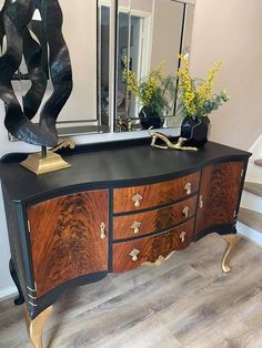 a black and gold sideboard with flowers on it in front of a large mirror