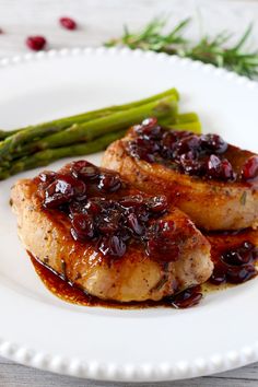 two pork chops with cranberry sauce and asparagus on a white plate