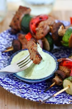 a blue and white plate topped with skewers of meat and veggies