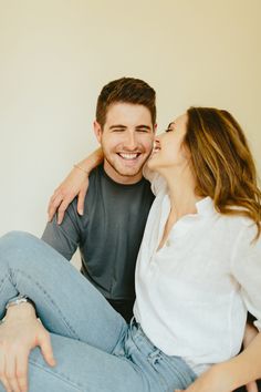 a man sitting next to a woman on top of a white bed kissing her cheek