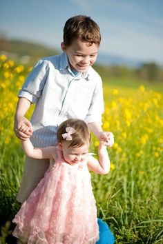 two young children playing in a field of flowers with one holding the other's hand