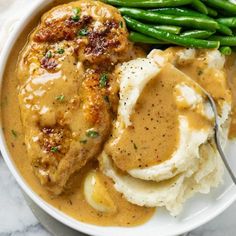 a white plate topped with mashed potatoes and meat covered in gravy next to green beans