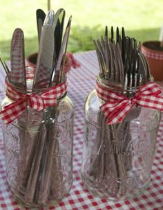 two mason jars with forks and spoons in them sitting on a checkered table cloth