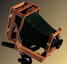 an old fashioned camera sitting on top of a tripod with a wooden case and lens