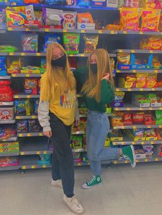 two girls wearing face masks in front of shelves of candy and other snacks at a store