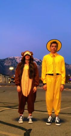 two people dressed in costumes standing next to each other on an airport tarmac with mountains in the background