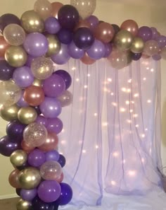 a purple and gold balloon arch with lights on the wall behind it for a birthday party