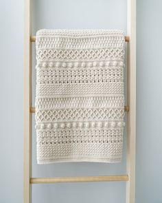 a white crocheted blanket hanging on a ladder in front of a blue wall