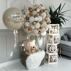 a teddy bear in a basket next to balloons and baby's name blocks on the floor