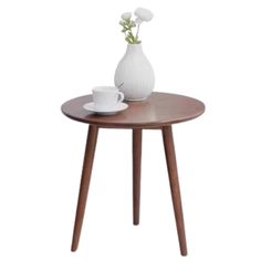 a white vase with flowers on top of a wooden table next to a cup and saucer