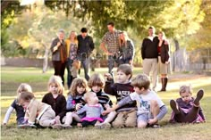 a group of children sitting on the ground in front of a tree with their parents