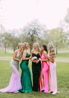 four women in long dresses standing next to each other on the grass with trees in the background