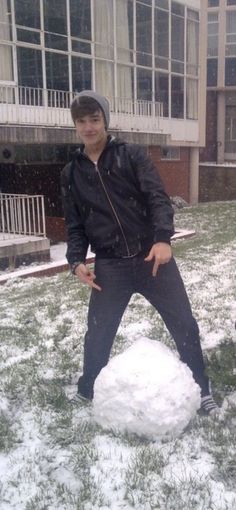 two men are playing in the snow with a snowman on the lawn near an apartment building