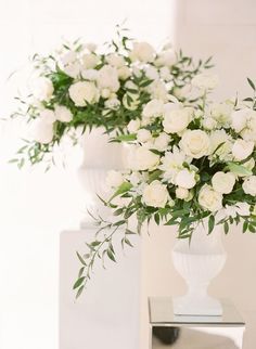 two white vases filled with flowers sitting on top of a table next to each other