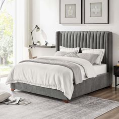 a bedroom with white walls and grey bedding, two framed pictures on the wall