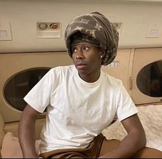 a young man sitting on top of a bed in front of dryer doors wearing a hat