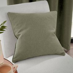 a light green pillow sitting on top of a white chair next to a vase with a plant