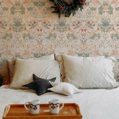 a bed with pillows and two mugs on it, next to a christmas wreath