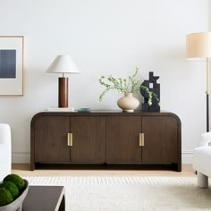 a living room with white couches and green plants on top of a wooden cabinet