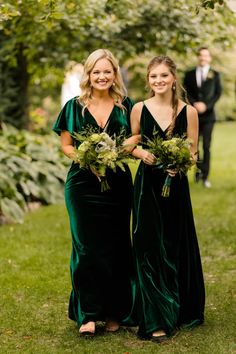 two women in green dresses standing next to each other on the grass with greenery