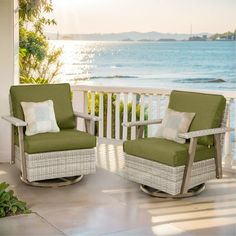 two wicker rocking chairs on a porch overlooking the ocean and water with green cushions